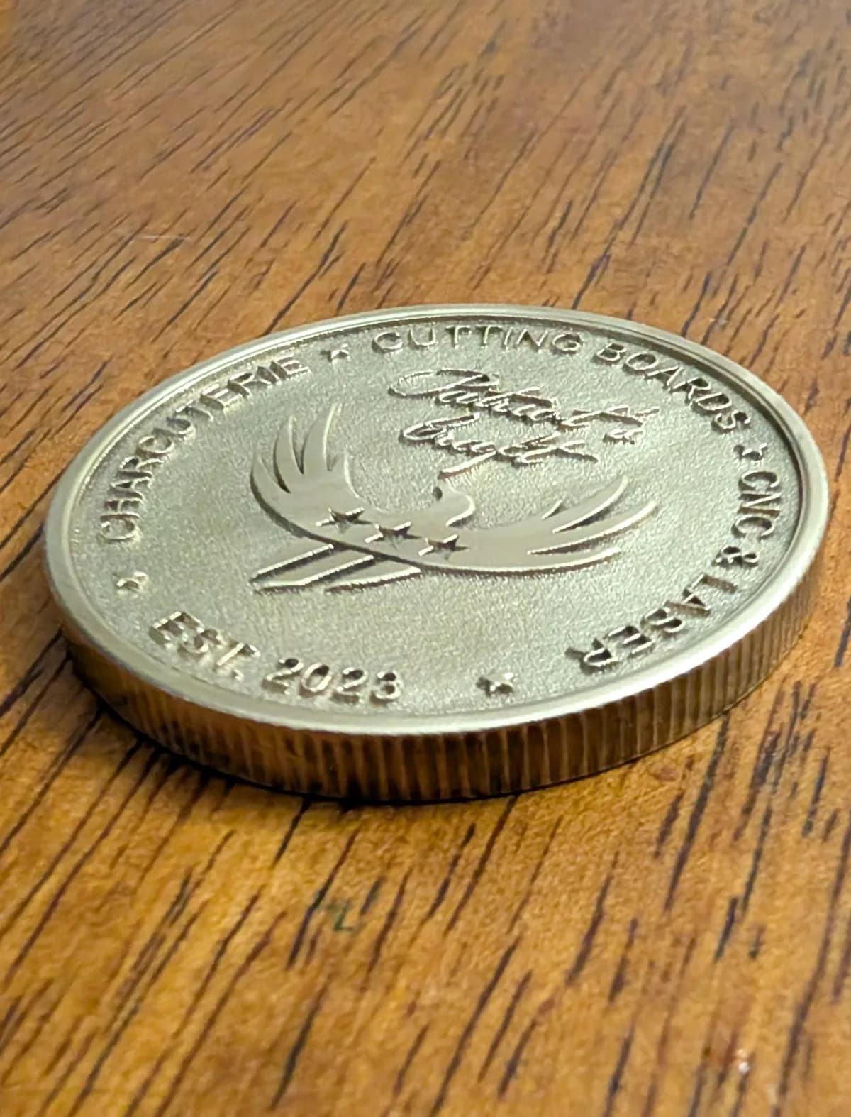 Brass round medallion with Patriot's Craft logo and text surrounding logo in a circle near the edge of medallion.